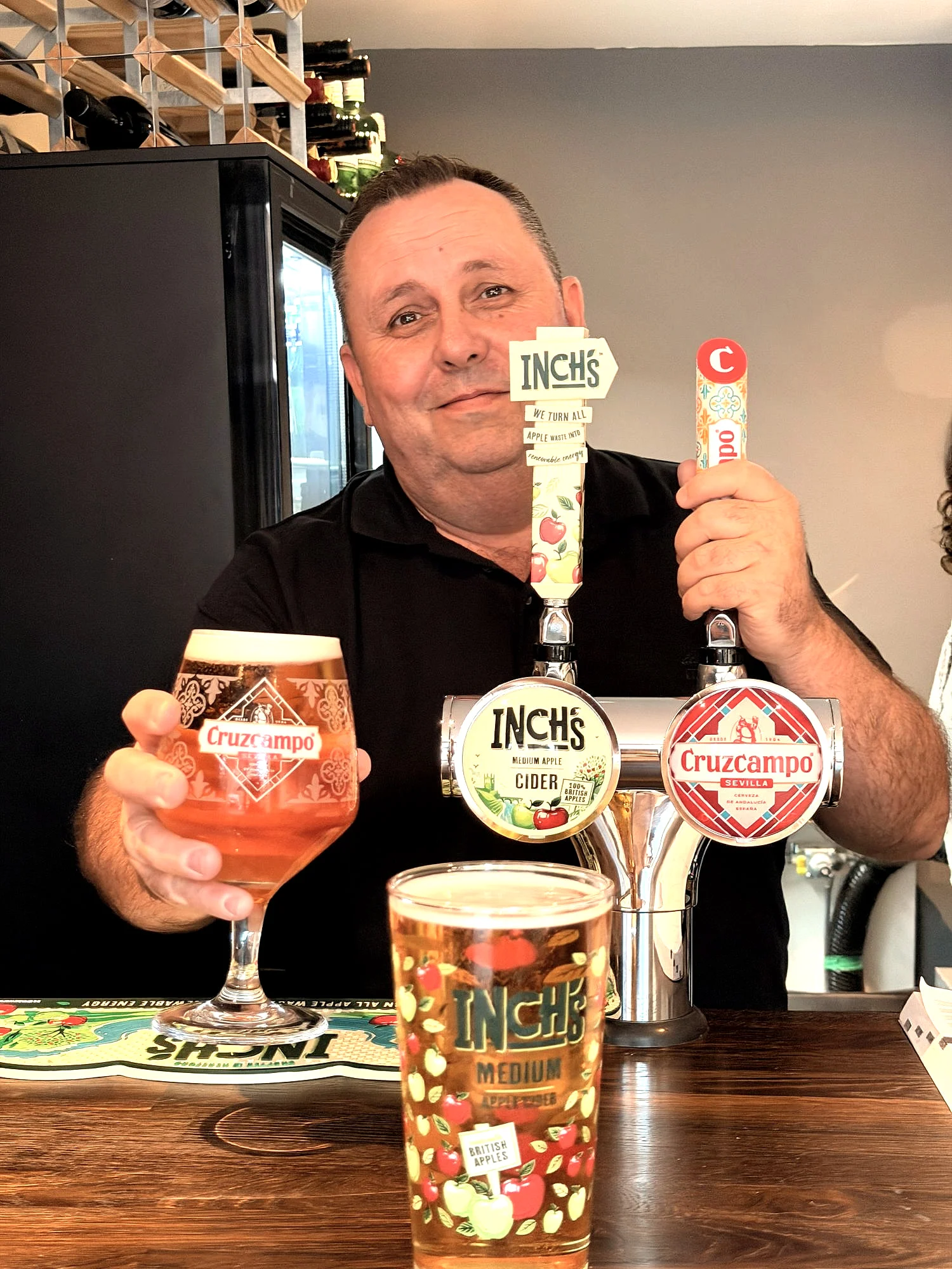 Behind the bar, holding a Cruzcampo next to the Inch's and Cruzcampo taps