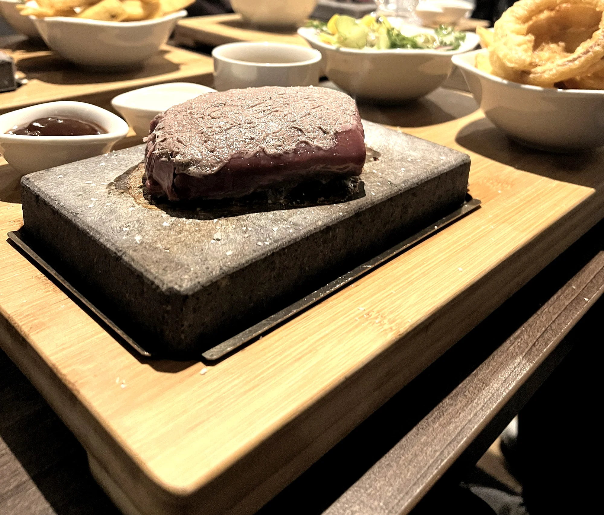 Steak on the stone with sauces, chips and onion rings around it