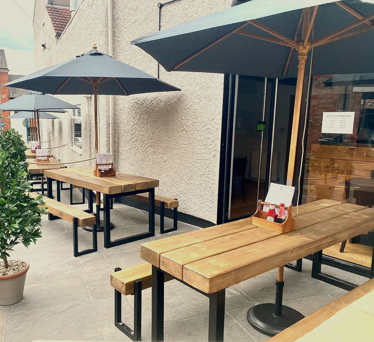 The terrace: wooden tables and benches under grey parasols